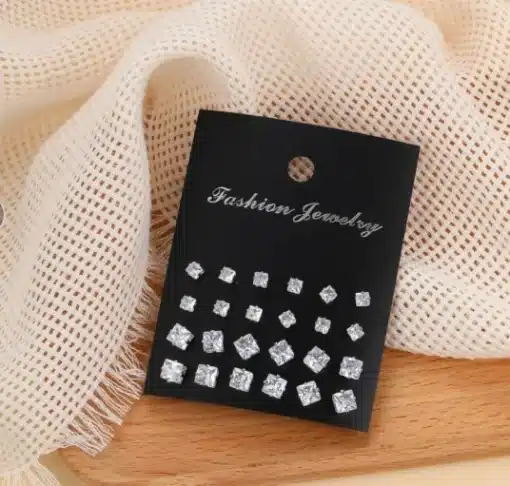 Erinevad kõrvarõngaste komplektid mustal kaardil, sisaldades mitmeid kristallidega kaunistatud kõrvarõngaid heledal kangal ja puidust taustal.