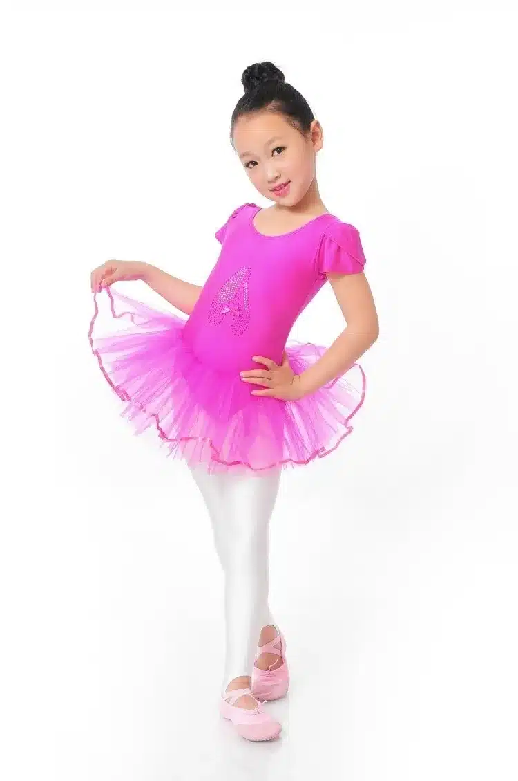 Tüdruk roosas Imekaunis balletikleidis, millel on õhuline tüllseelik ja lühikesed varrukad, valge taustal poseerimas.