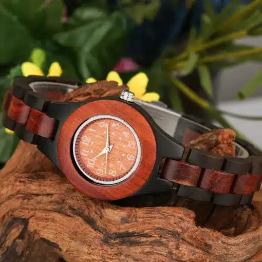 Puidust käekellad naistele | E-pood Tootemaailm Puidust käekellad naistele, millel on elegantne punakaspruun puidust korpus ja mustad detailid, asetatud looduslikule puidust taustale koos lilledega.