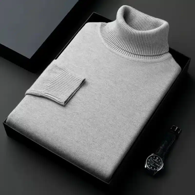 Hall klassikaline pullover kõrge kaelusega, volditud korrektselt karbis, rõhutades elegantset disaini. Pullover on valmistatud pehmest kangast, mis annab mugavust ja soojust. Taustal must pind ja käekell.