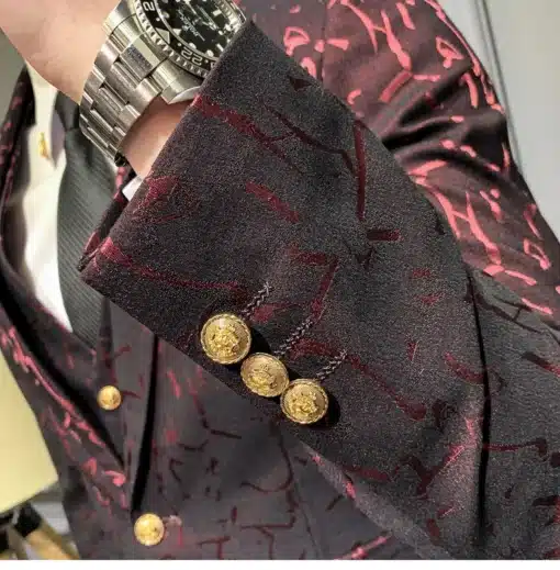 Elegantses keskkonnas demonstreeritakse tumepunast mustrilist ülikonda, millel on kuldsed nööbid ja keerukas muster. Ülikonda kantakse koos kella ja lipsuga, lisades üldisele stiilile luksust.