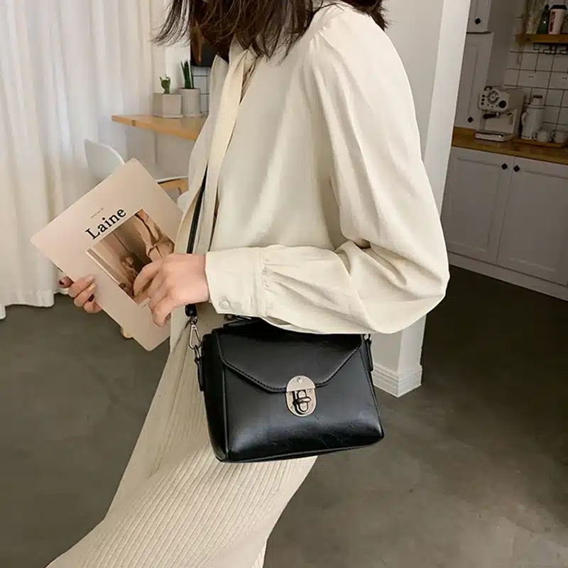 Naine kannab stiilset musta crossbody kotti sangaga, mis sobitub tema heleda riietusega. Koti minimalistlik disain sobib ideaalselt kaasaegsesse interjööri.