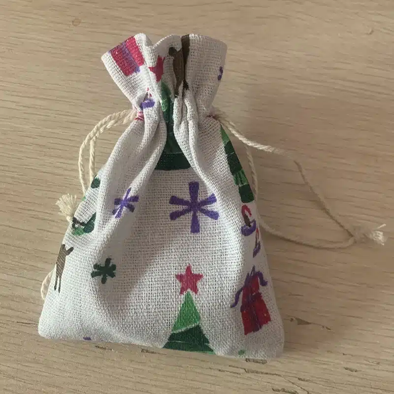 Väike lõuendkott puidu imitatsiooniga laual, täis Täringud jutustamise harjutamiseks komplekti täringuid. Kotil on värvilised kujundid ning tugev tõmbankeenõue.