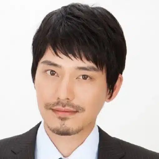 Mees kannab sirgete juustega parukat, esitledes lühikesi, musti sirgeid juukseid, mis loovad loomuliku välimuse. Taust on ühtlaselt hele, mis rõhutab soengu struktuuri ja stiili.