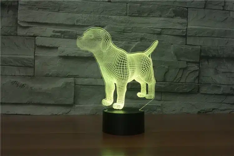 3D lamp 'Koer' valgusnäidik, millel on koera kolmemõõtmeline kuju, kumab soojas rohelises valguses ja paikneb tumedal alusel halli kiviseina taustal.