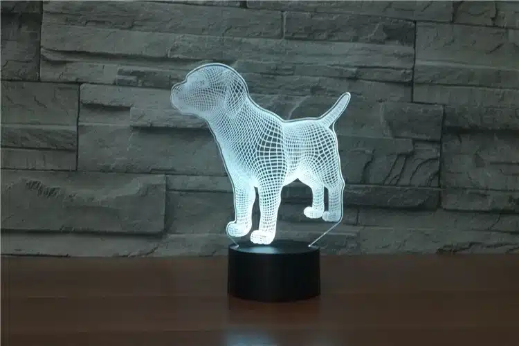 Kaasaegne ja dekoratiivne 3D lamp 'Koer', mis kuvab valgustatud koera kujutist musta aluse peal halli kiviseina taustal. Armas 3D efekt LED valgusega.