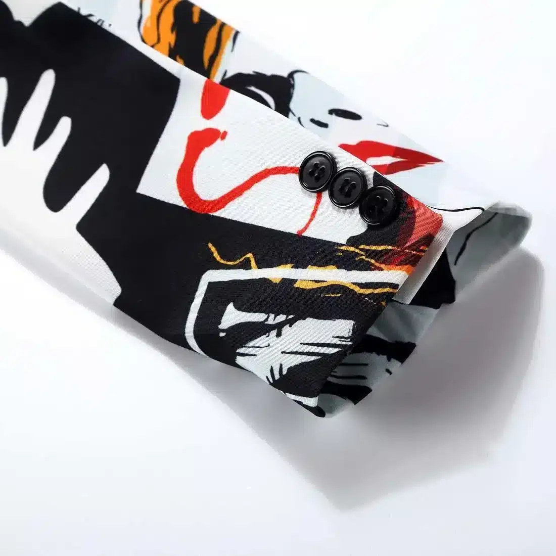 Piltidega pintsaku detail, mis näitab mustrilist kangast mustade, punaste ja valgete värvidega. Pintsakul on kolme nupuga varrukas ja abstraktne kujundus heledal taustal.