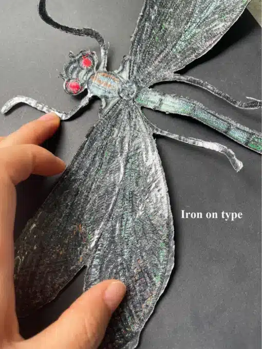 Suur pealetriigitav kiil mustal taustal. Detailne käsitöö kiil, millel on hall metallik sära ja erkpunased silmad, asetatakse ettevaatlikult triikimise ettevalmistuseks.