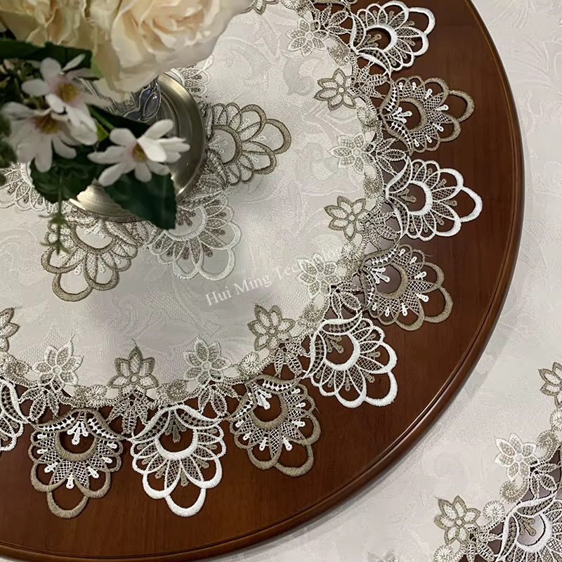 Ümmargusel puidust laual on elegantsed laudlinad lillelise pitsäärega. Peal on lilled metallvaasis, rõhutades valge kudumi delikaatset ilmet.
