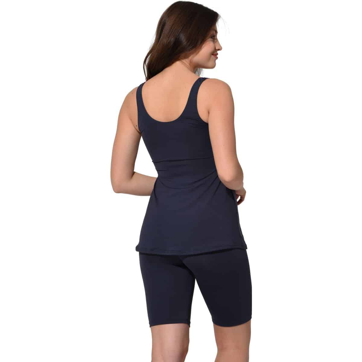 Naine seljaga tumedates toonides pikemad kaheosalised ujumiskomplektid seljas, millel on tank top ja pikad lühikesed püksid. Valge taust toob esile komplekti lihtsa ja elegantse stiili, sobides ideaalselt rannahooajaks ja ujumistreeninguteks.