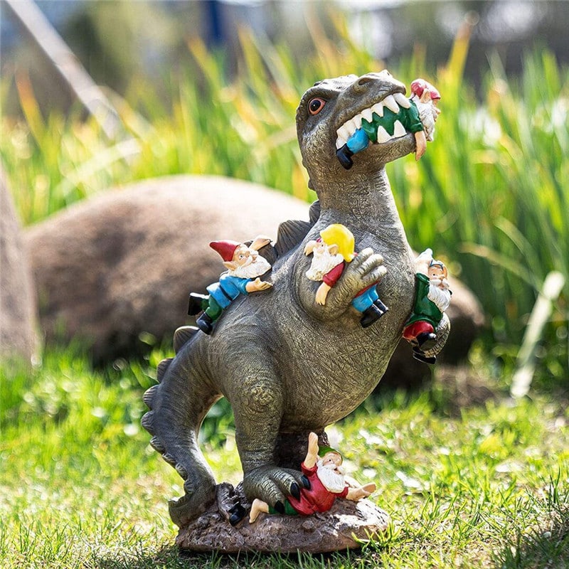 Dekoratiivne kuju dinosauruse ja pöialpoistega, hall dinoosaurus, mille seljas ja jäsemetel on värvikad pöialpoisid. Roheline muru ja kivine taust lisavad realistlikku välimust ning loovad lõbusa aiaelemendi.