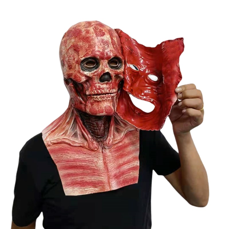 Inimene hoiab käes Kaks-ühes hirmutav maski, mis on valmistatud punastest ja beežidest toonidest, näidates anatoomiliselt detailset kolju. Mask lummab oma realistliku disainiga ning tekitab tõetruu hirmutava efekti. Taust on neutraalne, mis tõstab maski kontrasti esile.