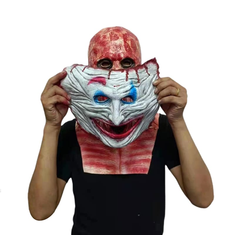 Kaks-ühes hirmutav mask, millel on veripunane pealisosa ja hirmuäratava klouniga eesosa, mida hoiab inimene käes musta tausta ees.