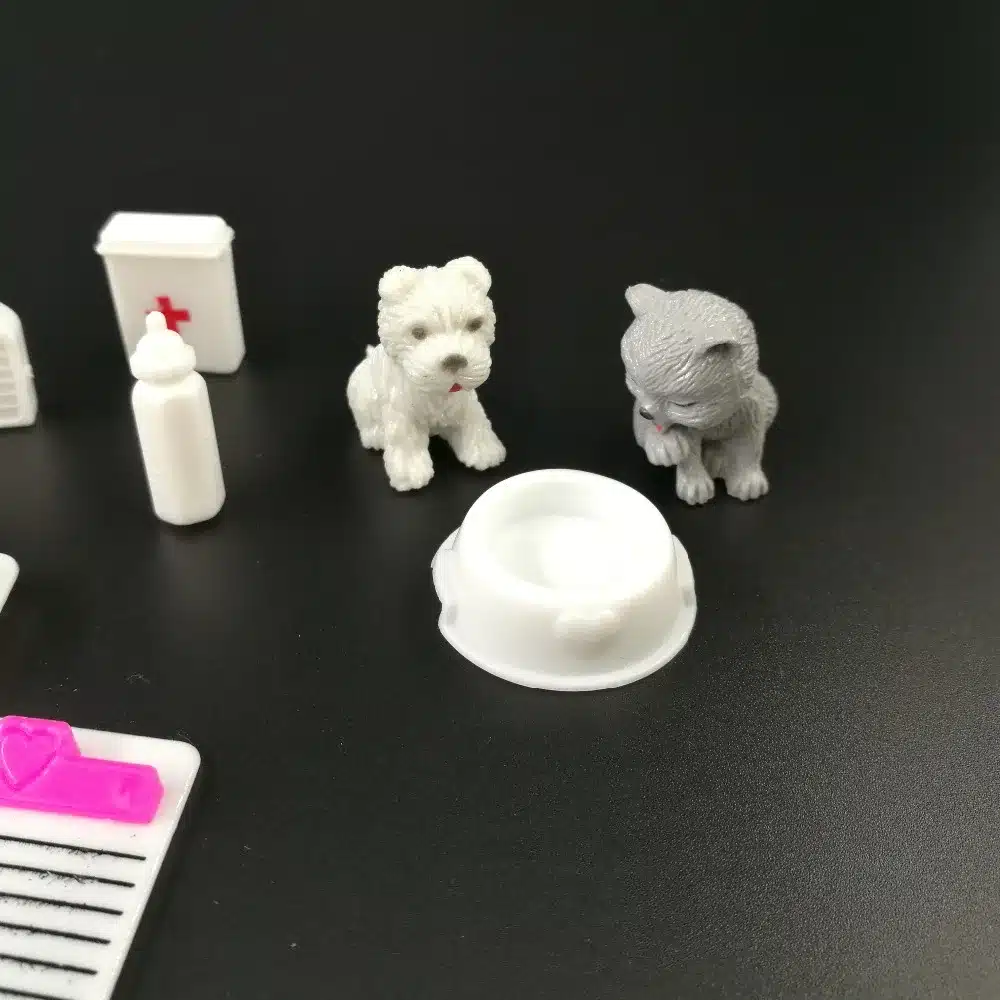 väikesed plastikust loomaarsti mänguasjad, sealhulgas koer, kass, toidukauss ja meditsiinilised tarvikud mustal taustal