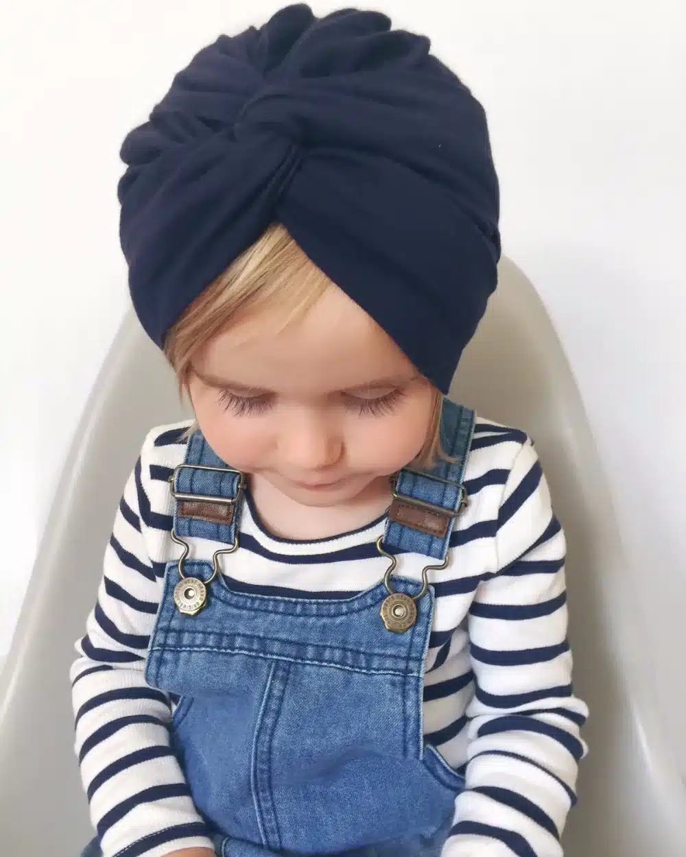 väike laps tumesinise turbanmütsiga, seljas triibuline särk ja teksapüksid