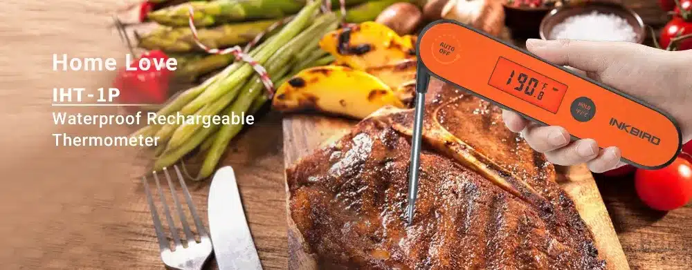 oranz digitaalne lihatermomeeter, millel on ekraan ja metallist sond, asetatud grillitud liha kohale
