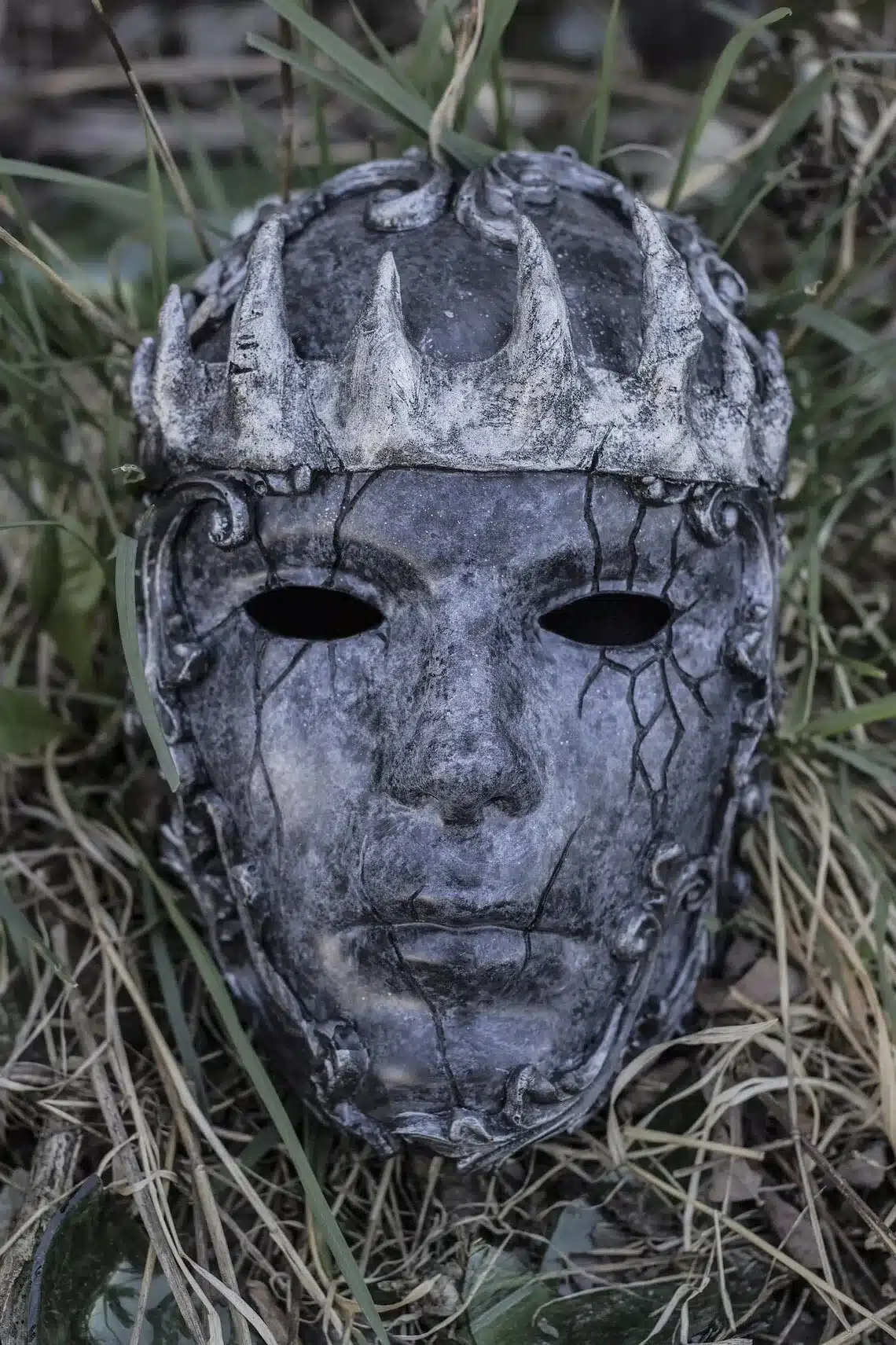 hall ja musta värvi kuningakrooniga mask, millel on pragunenud mustriga pind