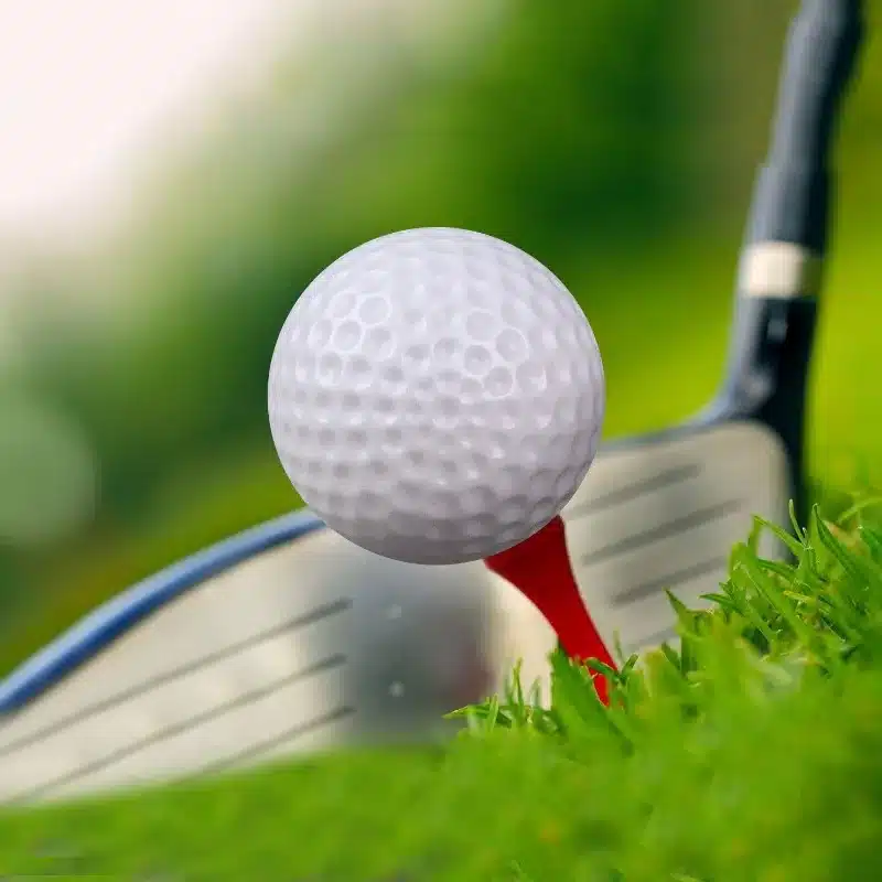 valge golfipall punasel tiil rohelisel murul, taustal golfikepp
