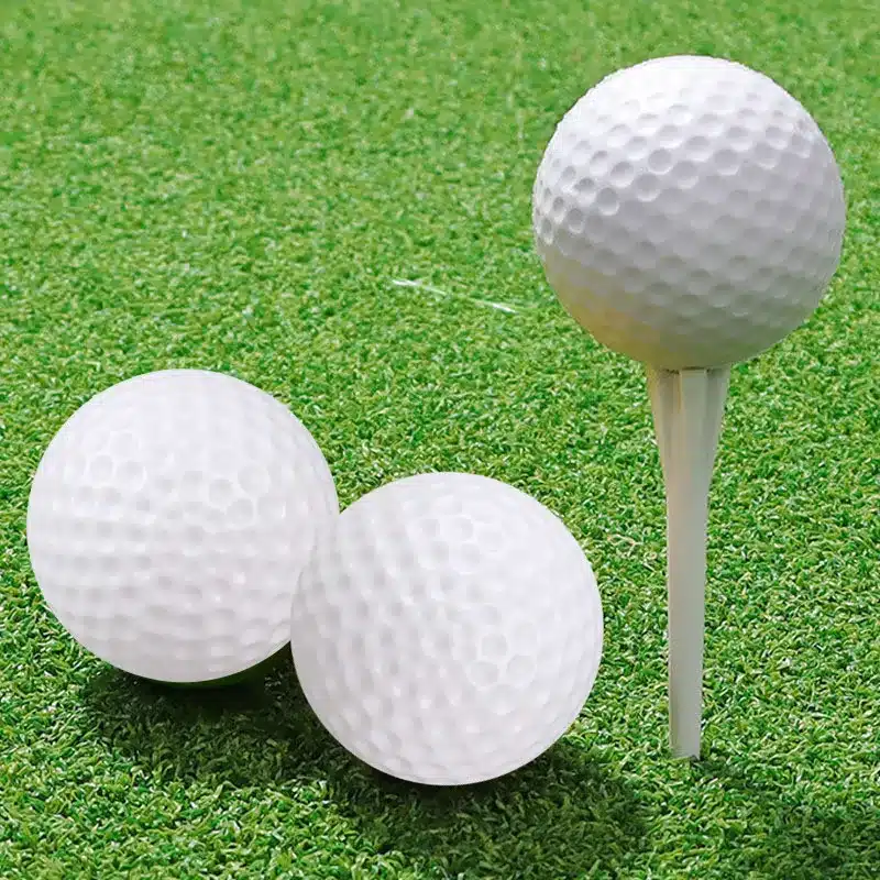 kolm valget golfipalli rohelisel murul, üks pall asetatud teele