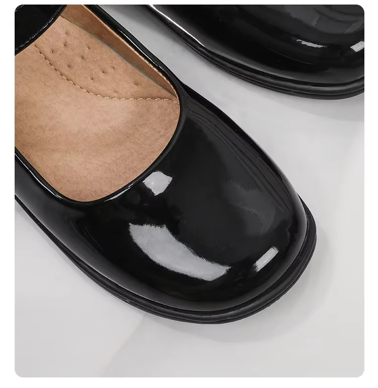 Läikivad mustad tüdrukute kingad beeži sisetallaga valgel taustal. Kingade pind on siledalt läikiv, rõhutades lihtsat ja elegantset disaini.