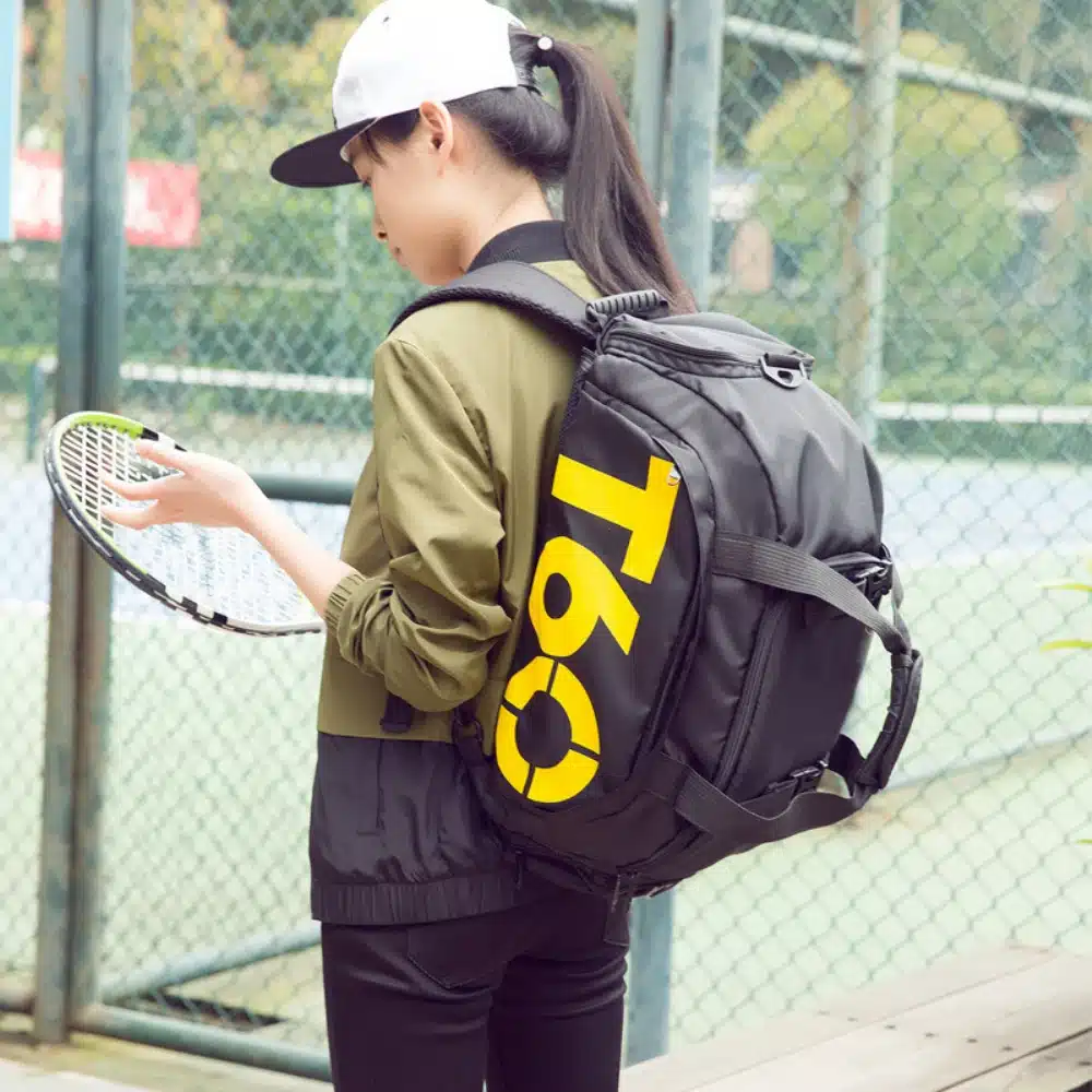 naine tennisereketiga, seljas must spordikott kollase kirjaga