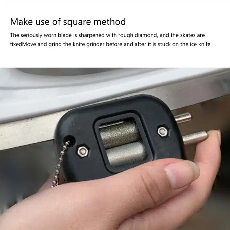 Käsi, mis hoiab musta plastist uisuteritajat, mis on kinnitatud metallist terale helehalli taustal.