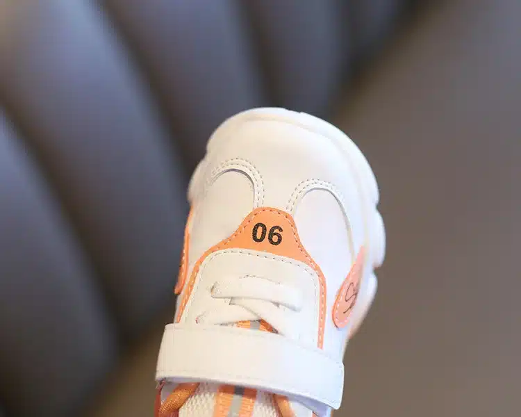 valge ja oranži detailidega laste toss, millel on numbriga kaunistus