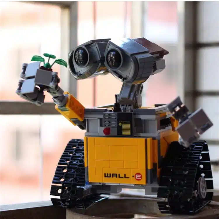 kollane ja hall robot, millel on suured silmad ja roomikud, hoiab käes väikest taime