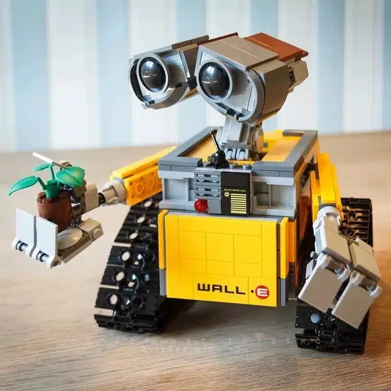 kollane ja hall robot, millel on suured silmad ja roomikud, hoiab käes väikest taime