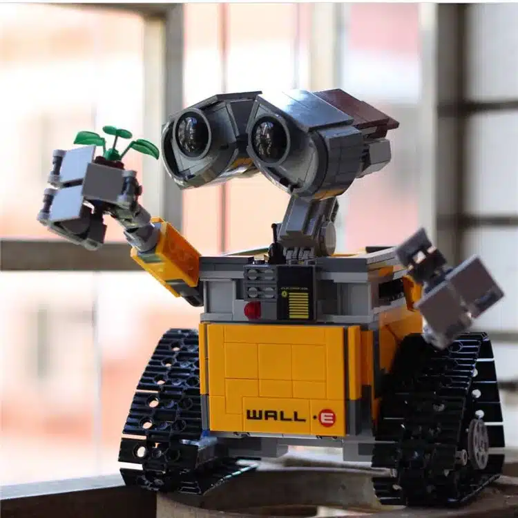 kollane ja hall robot, millel on suured silmad ja roomikud, hoiab käes väikest taime