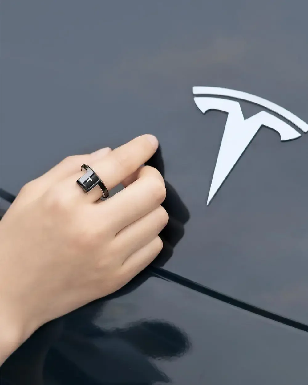 käsi kannab musta nutisõrmust, millel on valge logo, auto taustal