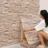 Naine paigaldab beige tooni 3D tapeeti, mille kivi muster loob realistliku ja kaasaegse interjööri. Tapeet on helisummutav ja veekindel, sobitudes ideaalselt igasse ruumi.
