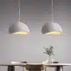 Kahe Skandinaavia stiilis LED laelambi paigutus söögilaua kohal minimalistlikus ruumis, hallid kuplid peene tekstuuriga, laual klaasvaas lilledega, taustaks hele sein.