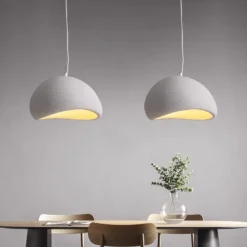 Kahe Skandinaavia stiilis LED laelambi paigutus söögilaua kohal minimalistlikus ruumis, hallid kuplid peene tekstuuriga, laual klaasvaas lilledega, taustaks hele sein.
