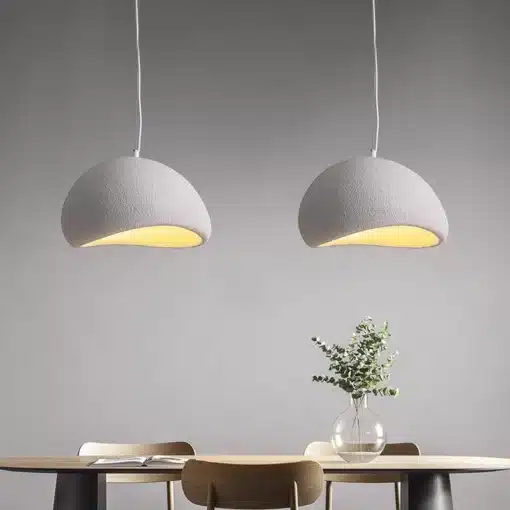 Kahe Skandinaavia stiilis LED laelambi paigutus söögilaua kohal minimalistlikus ruumis, hallid kuplid peene tekstuuriga, laual klaasvaas lilledega, taustaks hele sein.