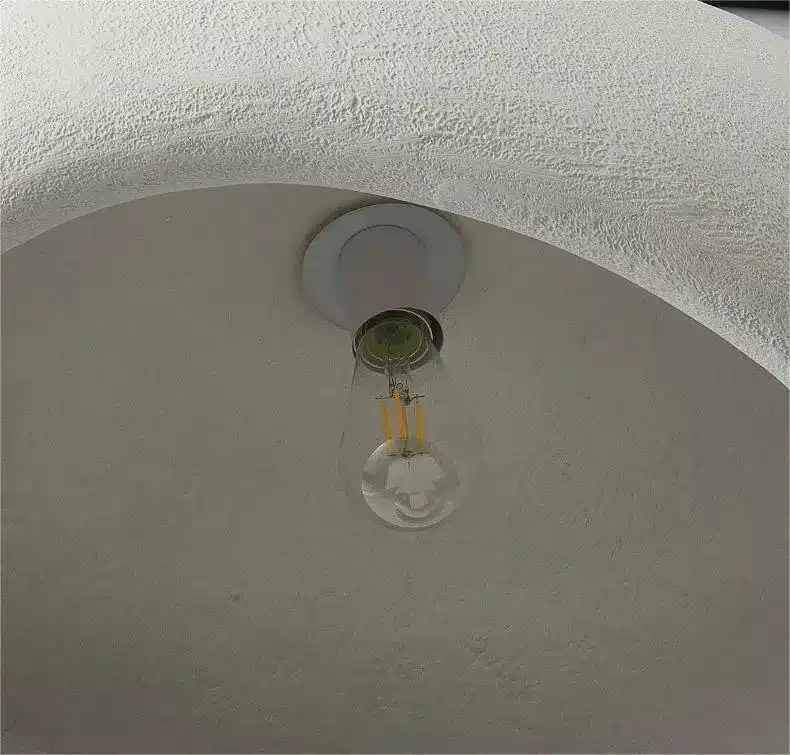 Lakitud valge laelamp koos läbipaistva klaasist LED-pirniga, mis on kinnitatud heledale kaarjale lakke, peegeldades skandinaavia disaini minimalismi.