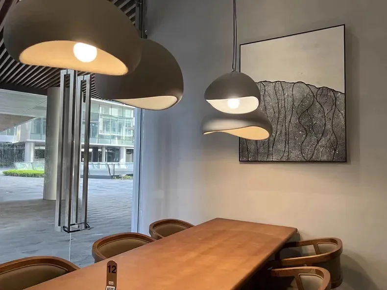 Kolm halli Skandinaavia stiilis LED laelampi ripuvad modernses kontoriruumis, valgustades pikka puidust koosolekulauda ja kunstipärase seinapildiga tausta.