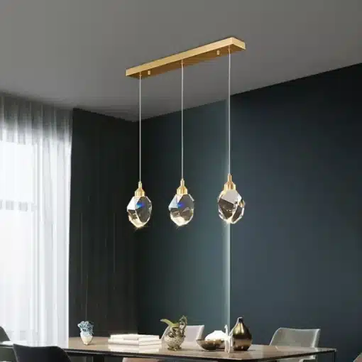 Kolm luksuslikku kristallidega ripplampi koos kuldsete riputustega rippumas elegantse söögilaua kohal, uhkeldades oma säravate LED-valgustitega tumedal taustal, Luksuslikud kristallidega ripplambid.