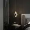 Stiilne luksuslik kristallidega ripplamp, mis ripub kaasaegse öökapi kohal tumedas ja elegantses magamistoas. Lamp peegeldab pehmelt valgust, luues sooja ja kutsuva atmosfääri.