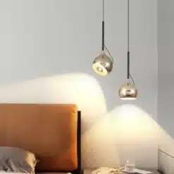 Kaasaegne energiatõhus LED ripplamp minimalistlikus magamistoas, kahe metallikviimistlusega lambi paigutusega voodi kõrval, loob sooja ja elegantse valgustuse rahulikul taustal.