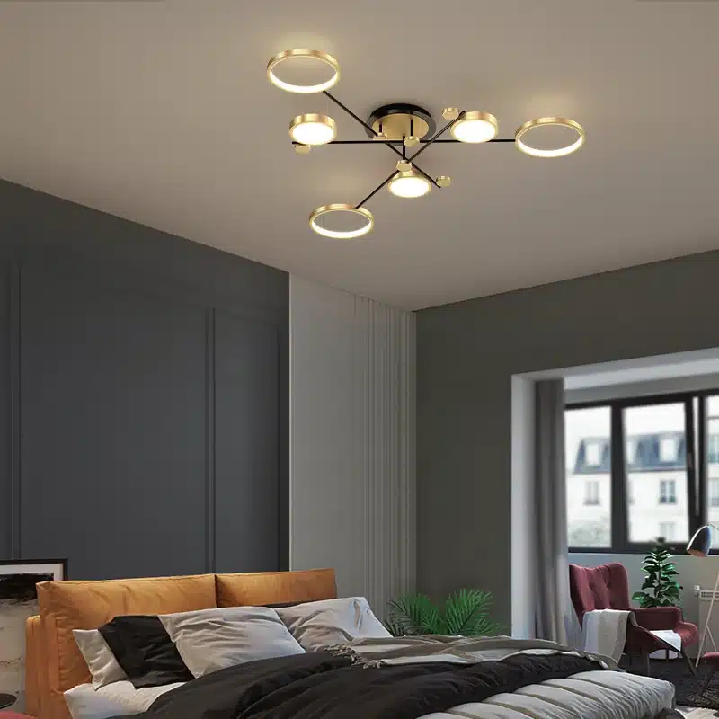 Kaasaegne magamistuba, kus lakke on paigaldatud luksuslik puldiga LED laelamp. Valgustil on kuldsed ringikujulised valgustuselemendid ja mustad varred, mis harmoneeruvad pehme neutraalse sisekujundusega.