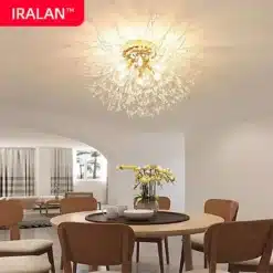 Luksuslik, elektrit säästev kristalllühter, mis ripub stiilse maitsva söögitoa lae all. Goldne toon ja säravad kristallid loovad elegantse ja sooja atmosfääri heledas ruumis moodsate puidust toolide ja ümmarguse laua kohal.