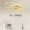 Kaasaegne stiilne LED laelamp kuldsete ringidega helendamas avaras elutoas minimalistliku mööbli taustal. Stiilne LED laelamp magamistuppa või elutuppa täiendab ruumi elegantselt.