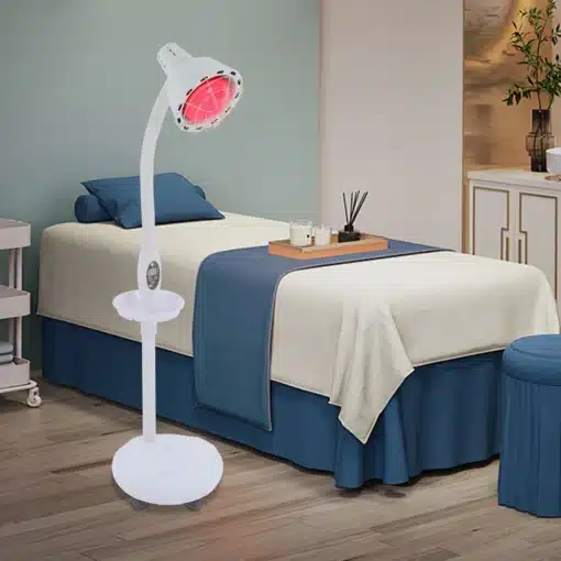 Võimas infrapuna füsioteraapia lamp valu leevendamiseks | E-pood Tootemaailm Ruumis seisab võimas infrapuna füsioteraapia lamp, valge korpuse ja reguleeritava varrega. Lamp kiirgab sooja punast infrapuna valgust, mis suunatud ühere uuele voodile taustal, sinise tekiga kaetud ning maitsekalt sisustatud.
