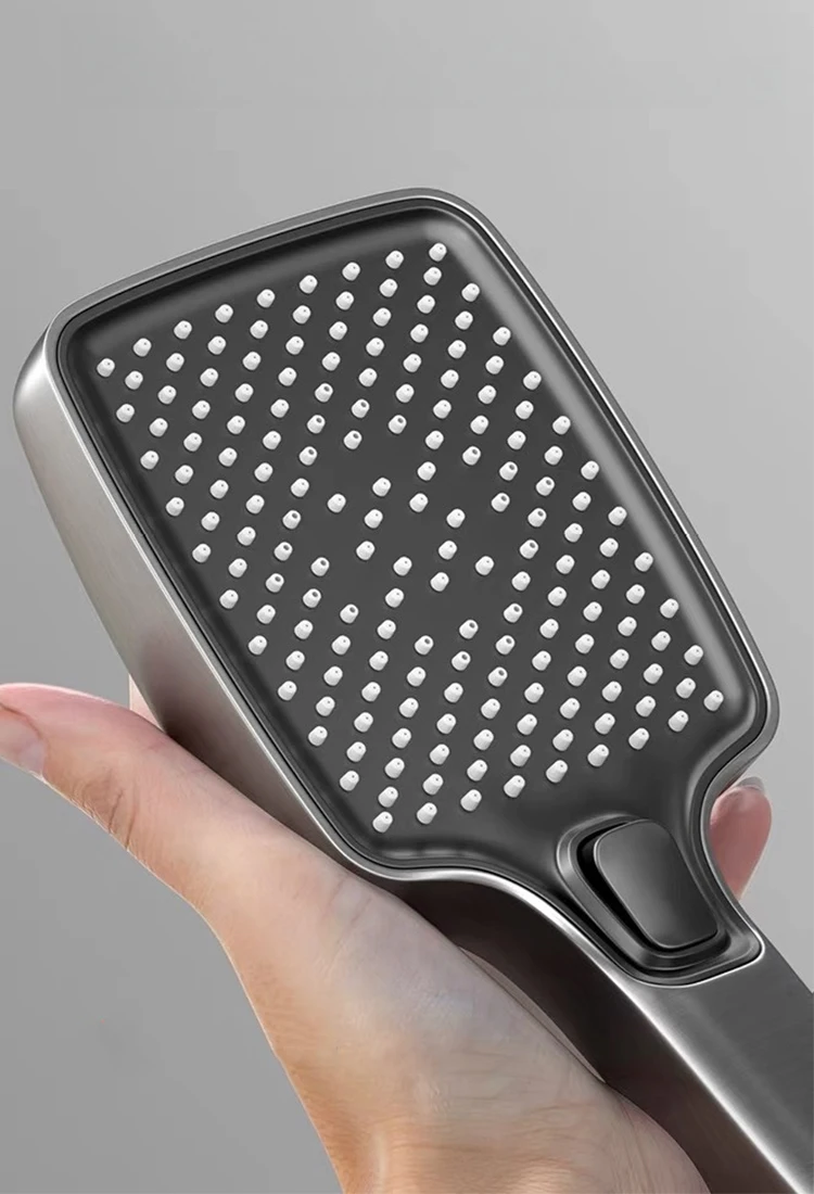 Inimene hoiab halli ja musta värvi nutikat digitaalset dušisüsteemi, millel on arvukalt väikseid düüse siledal pinnal. Taust on neutraalse tooniga.