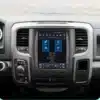 Dodge RAM CarPlay multimeediakeskus autosalongis, milles on keskne ekraan koos menüüikoonidega. Hall armatuurlaud ja nuppudega juhtpult loovad modernse ilme. Taustal on nähtav hägune maantee.