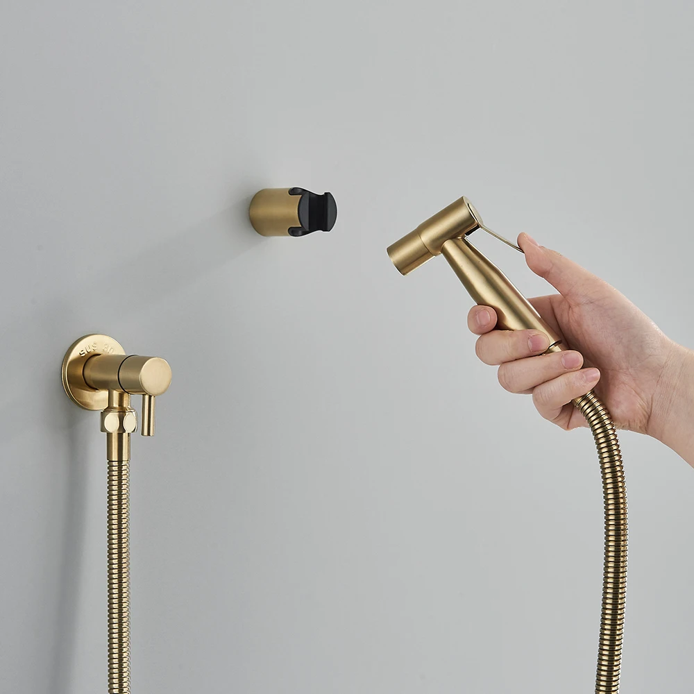 Käsitsi hoitav terasest seinale kinnitatav käimla bidet pihusti, elegantse kuldse viimistlusega, kinnitatuna neutraalsele hallile seinapinnale. Pihusti metallist voolik kaarub seina kõrval.