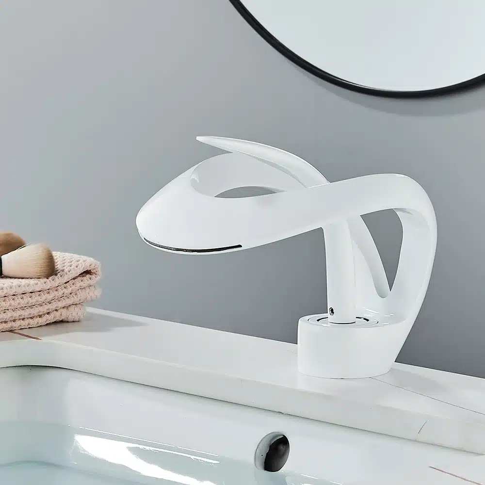 Stiilne valge vannitoa segisti, mille kaasaegne ja voolujooneline kuju paistab halli tausta ja valge kraanikausi peal. Kuldne luksuslik disain võimaldab nii kuuma kui külma vee kasutamist, tuues ruumi elegantsi.