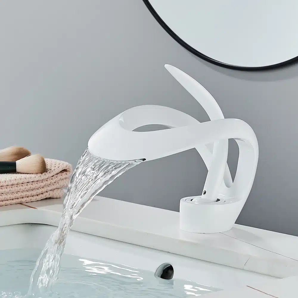 Vannitoa segisti kuldne luksuslik disain elegantse voolava veega, paigaldatud valge vannitoa valamule, halli seina taustal ja elegantse peegli kõrval.