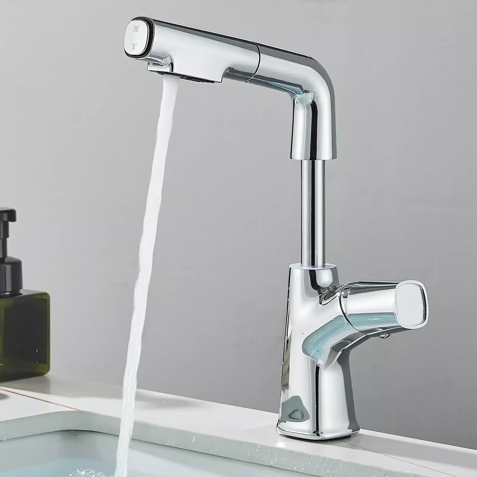 Kroomitud köögisegisti reguleeritava väljatõmmatava otsikuga, mis on kinnitatud valgele köögivalamule halli seina taustal, vesi voolab sujuvalt alla.